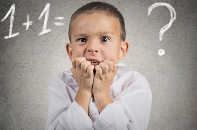 Image of child looking afraid to calculate 1 +1 equation on the board in the background.